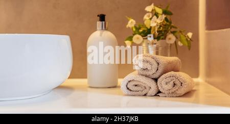 Handtücher Rollen auf, Seifenspender und weißes Waschbecken auf einem Tisch, Banner. Moderne Inneneinrichtung im Bad. Stockfoto