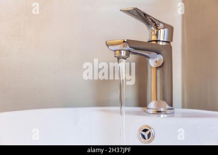 Waschbecken Wasserhahn, Badezimmer Inneneinrichtung Detail. Öffnen Sie die Chrom-Mischbatterie mit fließendem Wasser auf dem weißen Porzellanwaschbecken. Modernes Design Stockfoto