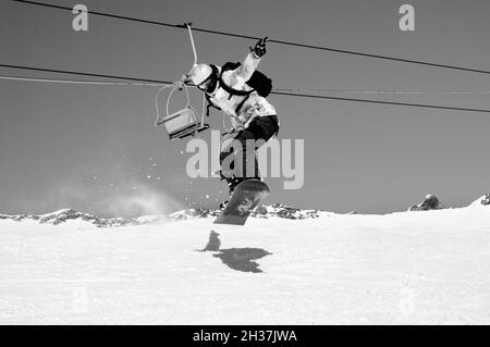 Snowboarder springen auf verschneite Skipiste, alter Sessellift. Kaukasus-Berge in sonnigen Wintertag, Region Dombay. Schwarz-Weiß-Retro-Bild. Hoch Stockfoto