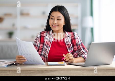 Heimbüro. Lächelnde Junge Asiatische Geschäftsfrau, Die Mit Papier Und Laptop Arbeitet Stockfoto