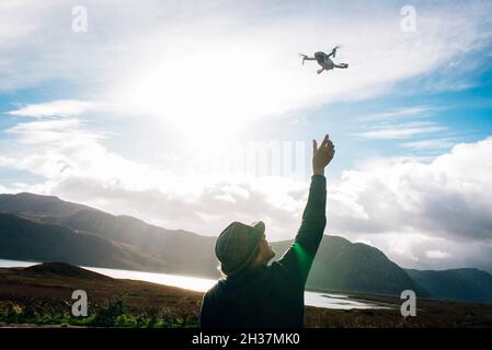 Ein Mann, der eine Mini-mavic-Drohne über die NC 500-Route im schottischen Hochland mit Bergen und einem See im Hintergrund fliegt. Speicherplatz kopieren Stockfoto