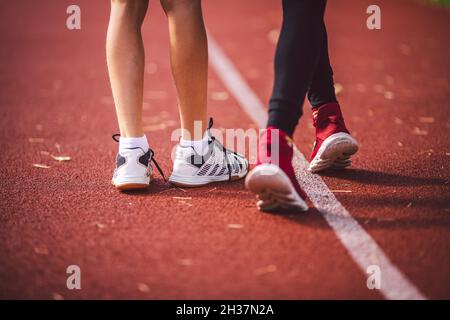 Vier Beine Nahaufnahme Bruder und Schwester in Turnschuhen laufen auf dem roten Laufband in der Laufstadion-Rückansicht. Zwei Läuferkinder nebeneinander auf der Rennstrecke Stockfoto