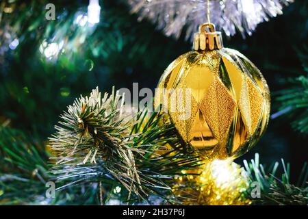 Schöne goldene Kugel auf geschmücktem Weihnachtsbaum mit silberner Lametta Girlande. Selektiver Fokus. Weihnachtskarte mit Dekorationen für den Silvesterabend Stockfoto