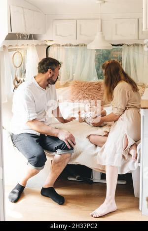 Familie mit Baby auf dem Bett im Anhänger am Morgen. Neugeborenes Kind, das im Wohnmobil mit den Eltern reist. Blick vom Van innen Stockfoto