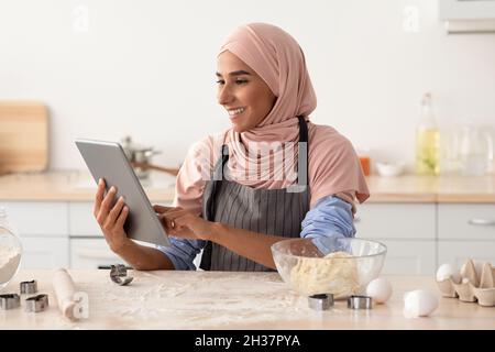 Schöne Islamische Hausfrau In Hijab Mit Digitalen Tablet In Der Küche Beim Backen Stockfoto