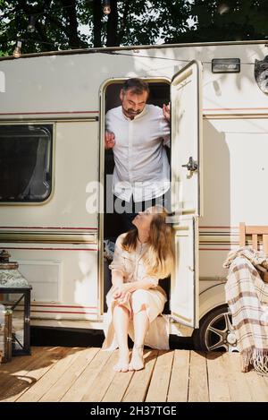 Camping und Reisen. Glückliches Paar, das sich draußen in der Nähe des Anhängers entspannt Mann und Frau auf ihrem Roadtrip Stockfoto