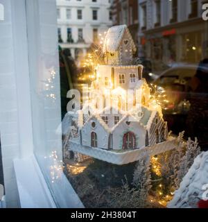 Hausgemachtes Lebkuchenhaus und weihnachtliche Gewürze mit Ornament. Reflexionen in einem Schaufenster Stockfoto