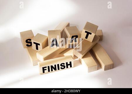 Die Wörter Start und Finish sind auf Holzblöcken und einem weißen Hintergrund geschrieben. Stockfoto