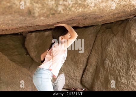 Ein kleines schönes Mädchen hält einen großen Stein in ihren Händen über ihrem Kopf. Das Kind hält sich an die Spitze der Höhle Stockfoto