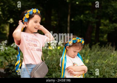 Zwei lustige kleine Mädchen mit ukrainischen Volksverzierungen auf dem Kopf. Kleines Kind, das in einem Sommerpark lacht Stockfoto
