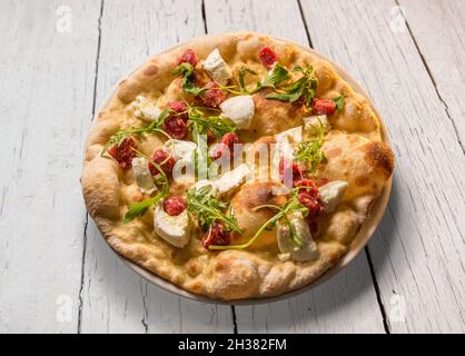 Pizza mit Mozzarella-Käse, Rohwurst und Rucola in Teller auf weißem Holztisch Stockfoto