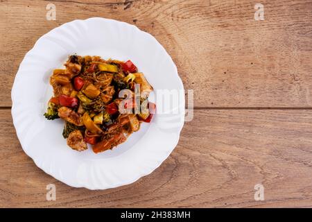 Yakisoba mit Hühnerfleisch in weißer Schale auf Holztisch. Stockfoto