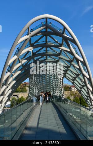 Tiflis, Georgien - 24. Oktober 2021: Die Brücke des Friedens, bogenförmige Fußgängerbrücke über den Fluss Kura in der georgischen Hauptstadt. Stahl und Glas Stockfoto