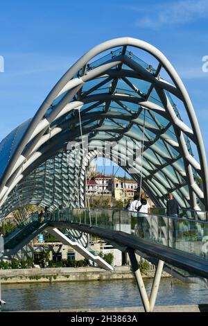 Tiflis, Georgien - 24. Oktober 2021: Die Brücke des Friedens, bogenförmige Fußgängerbrücke über den Fluss Kura in der georgischen Hauptstadt. Stahl und Glas Stockfoto