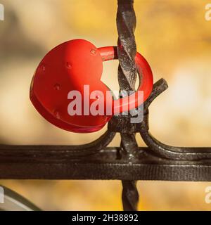 Rotes Schloss in Herzform auf schwarzem, altem Metallzaun, Liebessymbol, selektiver Fokus, verschwommener Herbsthintergrund Stockfoto