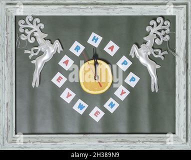 Imitation einer Uhr mit Zeigern und der Aufschrift Happy New Year anstelle von Zahlen mit dekorativen Hirschen in den Ecken in einem Holzrahmen Stockfoto