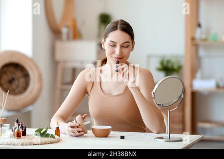 Junge Frau, die am Tisch sitzt und in der Flasche natürliches ätherisches Öl riecht Stockfoto