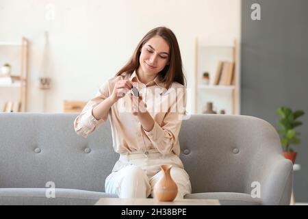 Junge Frau, die auf dem Sofa sitzt und eine Flasche ätherisches Öl im Zimmer öffnet Stockfoto