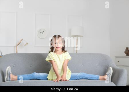 Kleines Mädchen, das zu Hause auf dem Sofa ein Bein gespalten hat Stockfoto