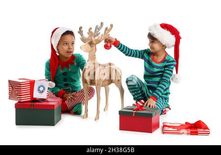 Kleine Jungen, die als Elfen gekleidet sind, schmücken Holzhirsche mit Weihnachtskugel auf weißem Hintergrund Stockfoto