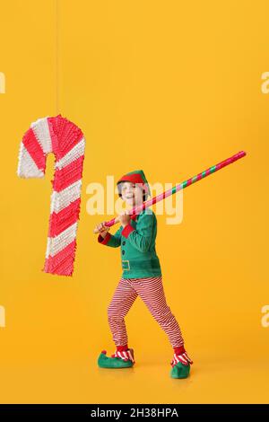 Niedlicher kleiner Junge, der als Elfe gekleidet ist, mit einer Pinata aus Zuckerrohr auf farbigem Hintergrund Stockfoto