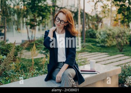 Müde Rotschopf Frau nimmt Ruhe im Park leidet an Nackenschmerzen sitzt auf der Bank Stockfoto