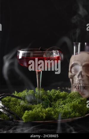 Halloween rot alkoholischer Cocktail und Totenkopf mit Rauch auf schwarzem Hintergrund. Horror lustiges Essen für die Nachtparty. Stockfoto