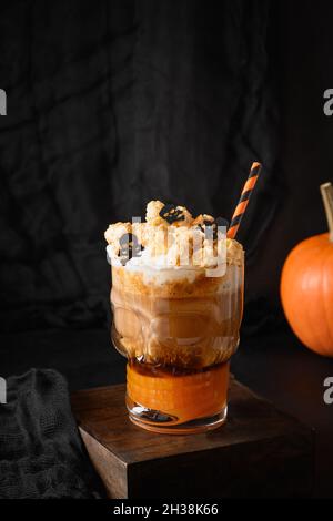 Halloween Kürbis Latte Kaffee mit Schlagsahne verzierten Totenköpfen und Popcorn in stilvoller Galss auf schwarzem Hintergrund. Stockfoto