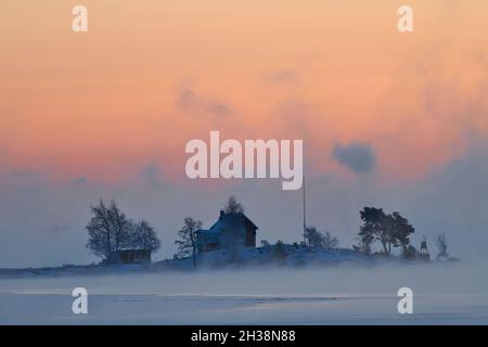 Helsinki, Finnland - 15. Januar 2021: Kleines traditionelles Häuschen auf einer eisigen Insel im Schärengarten von Helsinki, Finnland bei Sonnenaufgang bei extrem kaltem Sieg Stockfoto