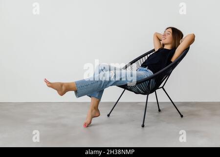 Junge hübsche Frau zu Hause sitzt auf modernen Stuhl vor dem Fenster entspannen in ihrem Wohnzimmer Stockfoto