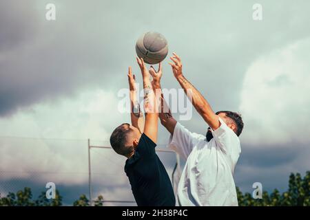 Zwei Freunde springen in der Luft, während sie gegen einen Basketball kämpfen Stockfoto
