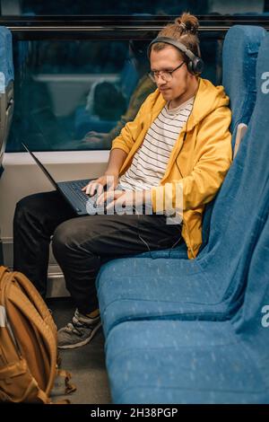 Junger Teenager-Mann mit Kopfhörern, reist, Programmierer arbeitet aus der Ferne. Stockfoto