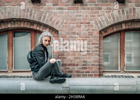 Frau sitzt in türkischer Pose auf einem Rohr in der Nähe eines verlassenen Backsteingebäudes Stockfoto