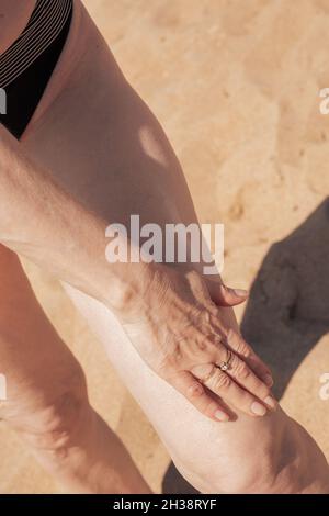 Reife Frau mit schlaffe Haut schmiert ihre Beine mit Sonnencreme. Schützt die Haut vor der strahlenden Sonne. Stockfoto