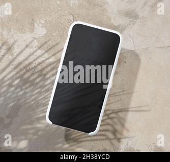 Smartphone auf beigefarbener Tischplatte mit Palmenblatt-Schatten, Draufsicht Stockfoto