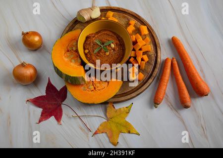 Herbstgerichte, Kürbissuppe Kochen. Kürbis auf einem Holzbrett, neben Zwiebeln, Karotten und Ingwer Stockfoto