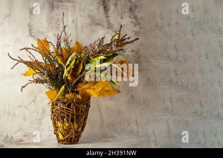 Herbst ikebana.Fall gelbe Kastanienblätter, Zweige mit wilden roten und violetten Blüten in einem Weidenkorb Stockfoto