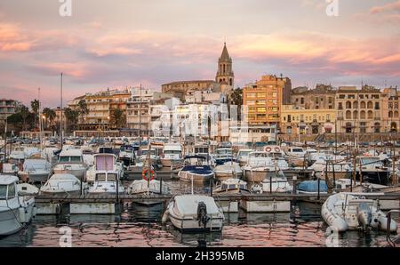 Sonnenuntergang mit dem goldenen Himmel der Stadt Palamós in Girona, Costa Brava, mit seinem charakteristischen Glockenturm und den Booten, die im Hafen festgemacht sind Stockfoto