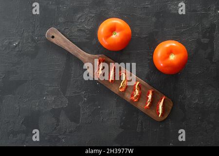 Rote, sonnengetrocknete Tomaten mit Sonnenlicht auf schwarzem Hintergrund. Leckere kleine Scheiben Tomate mit und Olivenöl. Stockfoto
