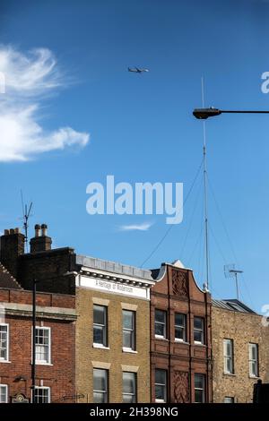 Ein Flugzeug fliegt über Gebäude in der Commercial Street, Spitalfields, im Osten Londons Stockfoto