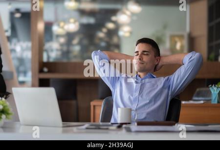 Entspannender, ruhiger kaukasischer Geschäftsmann, der sich am Schreibtisch ausruhen kann, nachdem er mit einem Laptop für Finanzen gearbeitet hat. Stockfoto