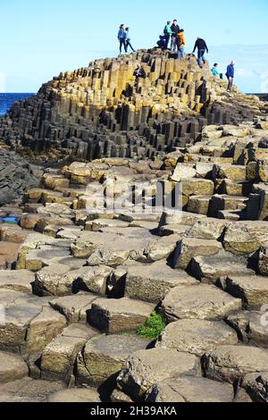 Besucher erklimmen am Giant’s Causeway in der Grafschaft Antrim an der Nordküste von Nordirland die Spitze natürlicher vulkanischer Felsformationen. Stockfoto