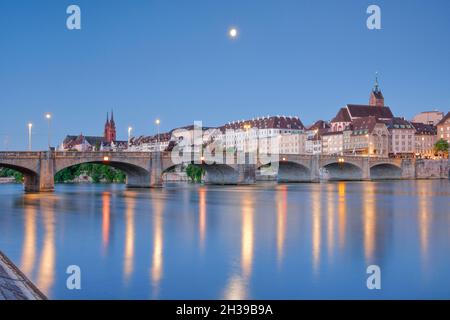 Blick vom Rheinufer entlang der Flusspromenade auf die Altstadt von Basel, die bei Nacht mit dem Basler Dom, St. Martin's, beleuchtet wird Stockfoto