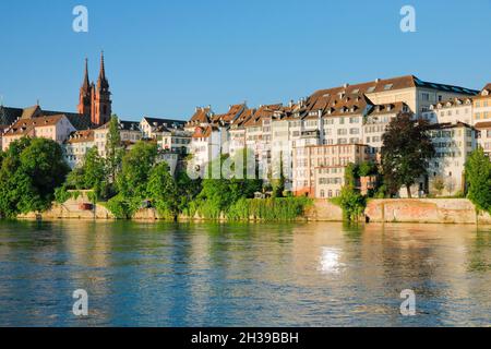Blick vom Rheinufer entlang der Uferpromenade auf den Basler Dom und die Altstadt von Basel mit dem Rhein im Vordergrund Stockfoto
