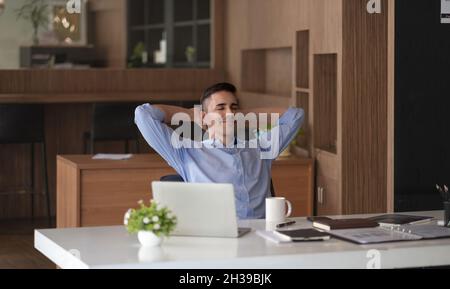 Entspannender, ruhiger kaukasischer Geschäftsmann, der sich am Schreibtisch ausruhen kann, nachdem er mit einem Laptop für Finanzen gearbeitet hat. Stockfoto