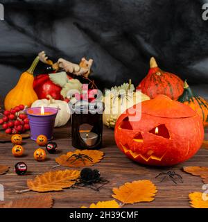 Halloween Kürbisse auf einem dunklen Holztisch mit Spinnen, Kerzen, Kürbissen, Blättern. Konzeptuelles Stillleben zum Thema Halloween. Stockfoto