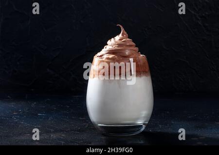 Dalgona kalter Kaffee in einem Glas auf schwarzem Hintergrund. Süßes koreanisches Getränk mit Instant-Kaffee und Creme mit Zucker Stockfoto