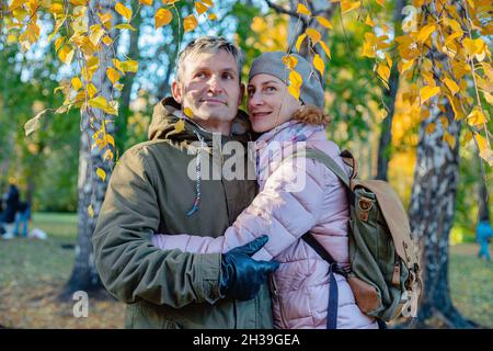 Glückliches Lächeln im mittleren Alter Paar im Freien. Attraktive Männer und Frauen kaukasischer Ethnie stehen umarmt. Herbstpark Hintergrund. Sonniger Herbsttag. Stockfoto