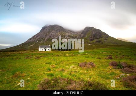 Schöne Landschaft von grünen Feldern, ein Haus unter hohen felsigen Bergen in Buachaille Etive Mor Stockfoto