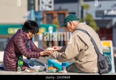 Ein asiatisches Senioren-Paar sitzt am sonnigen Herbsttag im Freien und picknickt gemeinsam in einem Park Stockfoto